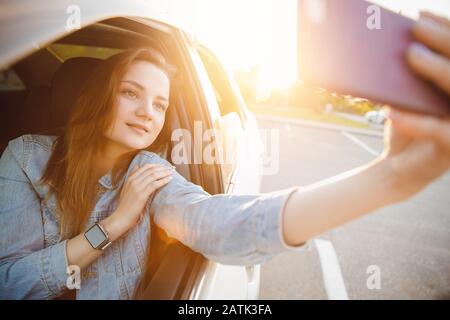 Selfie Foto des schönen Mädchens, das den Sonnenuntergang mit dem Auto treibt. Konzeptfahrerfahrt Stockfoto