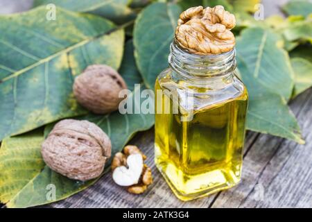 Nussöl in einem Glasbecher in der Nähe von Walnüssen und grünen Blättern auf einem Holztisch. Gesunde Ernährung. Stockfoto