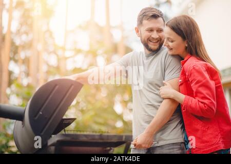 Fröhlicher Mann und junge Frau frittieren Fleisch auf dem Grillgrill im Naturgarten Stockfoto