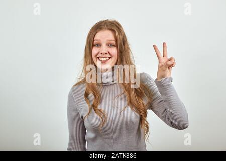 Frau im grauen Pullover glücklich mit guter Laune lächelt und zeigt ihre Finger zwei Stockfoto