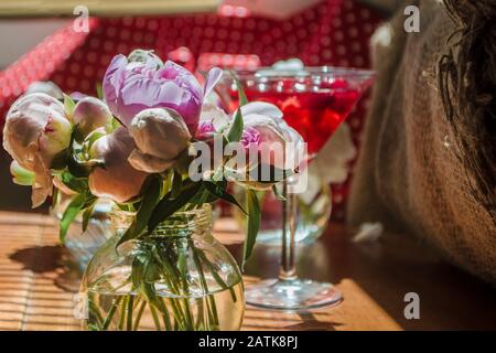 Wunderschöner kleiner Blumenstrauß unentdeckter Whitepink-Ponys vor dem Hintergrund eines roten Getränks in einer Dose. Knospen von Blumen stehen in einem kleinen Glasbecher Stockfoto