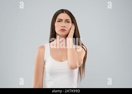 Junge kaukasier Frau in Weiß shirt über grauer Hintergrund berühren mit der Hand mit schmerzhaften Ausdruck isoliert, weil Ohrenschmerzen. Vorderansicht des Brünette an Kamera schaut. Stockfoto