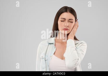 Junge kaukasier Frau in Weiß shirt über grauer Hintergrund berühren mit der Hand mit schmerzhaften Ausdruck isoliert, weil Ohrenschmerzen. Vorderansicht des Brünette mit geschlossenen Augen. Stockfoto