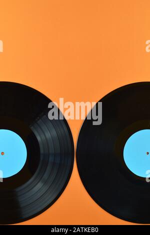 Zwei alte schwarze Schallplatten mit leeren zyanblauen Etiketten, die halb auf orangefarbenem Hintergrund stehen Stockfoto