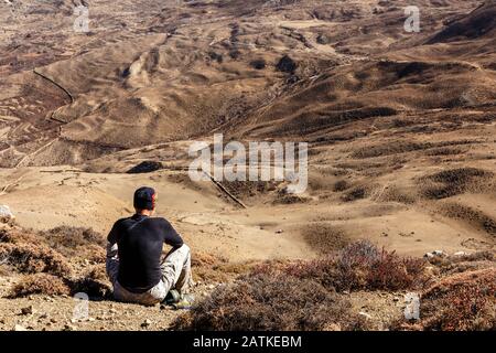 Ein Mann in einem schwarzen Hut sitzt auf einem Berg und blickt auf das Tal, den Himalaya, Nepal Stockfoto