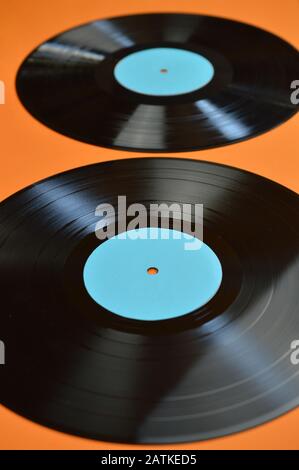 Zwei alte schwarze Schallplatten mit leeren zyanblauen Etiketten auf orangefarbenem Hintergrund Stockfoto