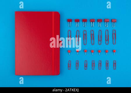 Red Business Notebook und Schreibwaren auf blauem Tisch. Zurück zur Schule oder zum Arbeitsplatz abstrakter Hintergrund. Minimale Zusammensetzung. Stockfoto