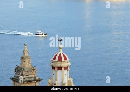 Das Pilotboot Valletta betritt den Grand Harbour, Malta, bei Sonnenschein am Abend, überblickend vom Turm und der Kuppel der Liessenkirchenkirche. Stockfoto