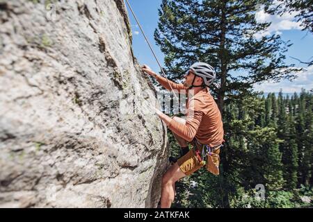 Der Mensch hält sich mit den Fingerspitzen an den Felsen, während er mit einem Seil klettert Stockfoto