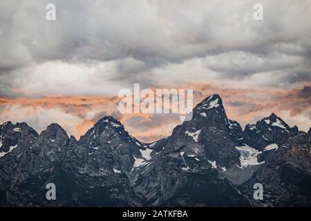 Untergehende Sonne reflektiert von Wolken hinter den Gipfeln der Tetons, Wyoming. Stockfoto