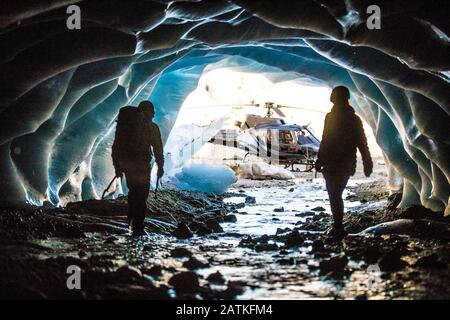 Abenteuerlustige Paare tauchen aus einer Eishöhle auf, um ihren Hubschrauber zu finden. Stockfoto