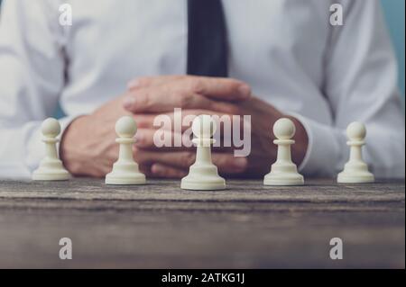 Geschäftsmann sitzt an seinem Schreibtisch mit fünf Pfandschachtstücken, die vor ihm positioniert sind. Konzeptionelles Bild von Beschäftigung und Führung. Stockfoto