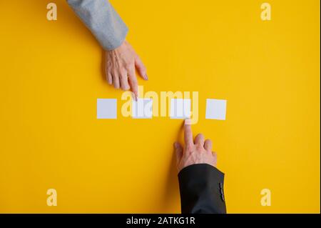 Hand des Geschäftsmannes und der Geschäftsfrau, die vier leere Post-IT-Papiere über gelbem Hintergrund platziert. Stockfoto