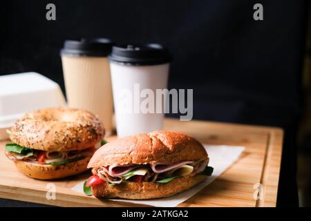 Köstliche klassische blt-Sandwiches mit Schinken, Käse, Speck und Tomaten. Frühstücks- und fast Food-Essenskiste mit Getränk auf isoliertem schwarzem Hintergrundwoode Stockfoto