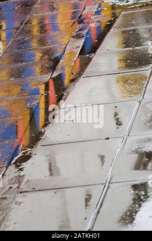 Urbaner Boden nach dem Regen spiegeln sich die Farben der Umgebung im nassen Boden wider und schaffen so ein interessantes Design Stockfoto