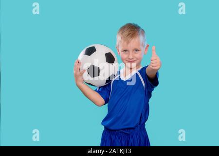 Glückliches kleines Kind in Sportbekleidung, das einen Fußballball auf blauem Hintergrund hält Stockfoto