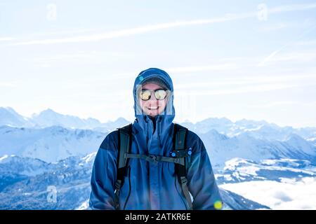 Bergsteiger Backpacker lächeln im Winter auf dem Gipfel gegen blaue verschneite Bergschichten, sonniger, blauer Himmel Stockfoto