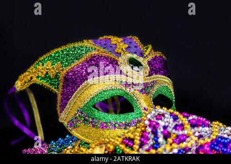 Nahaufnahme einer bunten Jester-Maske auf einem Bett aus bunten Perlen vor schwarzem Hintergrund. Seitenansicht. Stockfoto