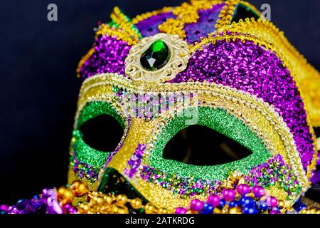 Bunte Jester-Maske auf einem Bett aus Festivalperlen. Nahansicht mit dunklem Hintergrund. Stockfoto