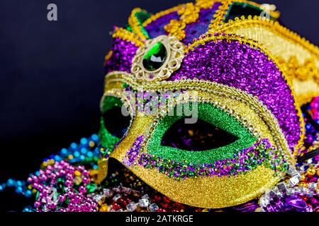 Nahaufnahme einer bunten Jester-Maske auf einem Bett aus Festivalperlen. Dunkler Hintergrund. Querformat zugeschnitten. Stockfoto