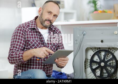 Mann mit Tablet-pc zur Reparatur der Waschmaschine Stockfoto