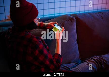 Smart jugendlicher Mädchen sitzt auf einem Sofa zu Hause spielen fps video Spiel auf Ihrem Smartphone, hält und nutzt Handy im horizontalen Modus "Landschaft" Stockfoto