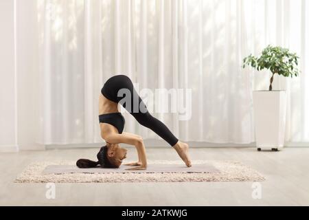 Junge Frau, die zu Hause einen Handstand auf einer Matte trainiert Stockfoto