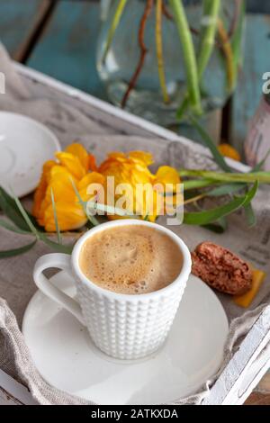 Nahaufnahme eines Frühstückskonzepts mit einer Tasse Kaffee im Vorderteil, einem Makaronstück neben dem Kaffeegericht und einem Paar Butterkuchen-Blumenlaie Stockfoto