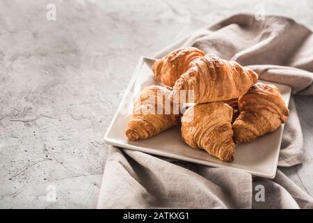 Frisch gebackene französische Croissants auf einem quadratischen Teller mit einer grauen Serviette auf hellgrauem Hintergrund. Köstliche Croissants zum Frühstück horizontal orienta Stockfoto