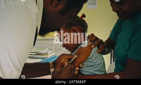 Melsisi, Pentecost Island/Vanuatu - 10. MAI 2019: Süßes junges schwarzes pazifikkind, das während einer ärztlichen Kontrolle durch eine Krankenschwester injiziert wird Stockfoto