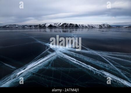 Winterlandschaft mit detailliertem kreuzenden Eismuster im Vordergrund auf einem zugefrorenen See. Baikalsee, Irkutsk, Sibirien, Russland. Stockfoto