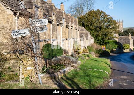 Wegweiser und Cotswold Steinhäuschen im Winter Sonnenlicht. Withington, Gloucestershire, England Stockfoto