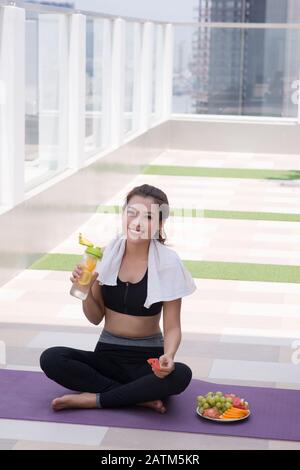 Junge Frau in stilvolle Sportswear sitzen und entspannen auf dem Boden mit Kunststoff Flasche Wasser nach dem Training auf dem Dach. Stockfoto