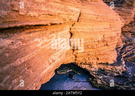 Unter den Strahlen der aufgehenden Sonne sind orangefarbene Sandstrandfelsen eingefärbt. Stockfoto