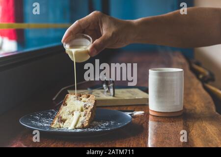 Der Mann gießt die Creme mit einer Tasse Kaffee auf dem Tisch In den Obstkuchen. Stockfoto