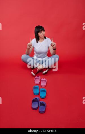 Frau mit den Fingern nach oben und bunten Flip-Flops. Loor mit Zeigefingern nach oben und bunten hellen Flip-Flops vor ihr. Stockfoto