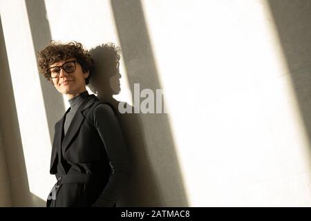 Inhaltsporträt attraktive junge Frau in schwarzem, formalem Kleid, das bei Sonnenlicht an der Wand steht Stockfoto