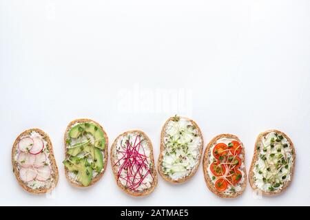 Flaches Layout mit verschiedenen Sandwiches mit Gemüse und Mikrogrüns auf weißem Hintergrund mit Platz für Text Stockfoto