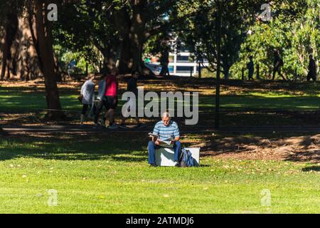 Sydney, Australien - 3. Juli 2016: Man liest die Zeitung auf einem Rasen auf dem Sydney Domain-Gelände Stockfoto