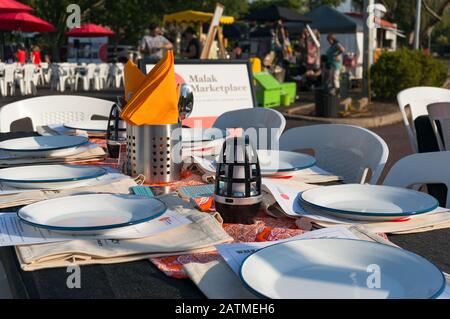 Darwin, Australien - 1. Juni 2019: Tisch zum Abendessen mit weißen Tellern und orangefarbenen Servietten auf dem Malak-Marktplatz in Darwin. Lokale australische Landwirte m Stockfoto