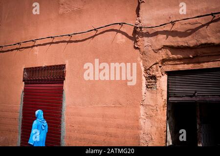 Eine Frau in blauer Kleidung geht an einer dunkelroten Tür in Marrakesch, Marokko, vorbei Stockfoto