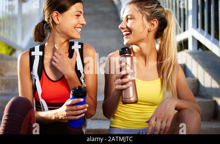 Schöne Frauen in Sportbekleidung Trinkwasser, sprechen und ruhen nach dem Training im Freien Stockfoto