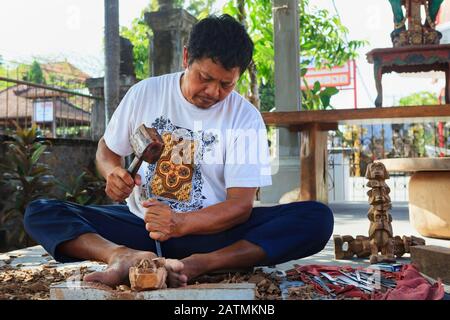 Dorf Ubud, Insel Bali, Indonesien - 10. Oktober 2016: Balinesischer Mann arbeitet hart im Holzladen. Andenken an traditionelle Kunst - Handschnitzen Stockfoto