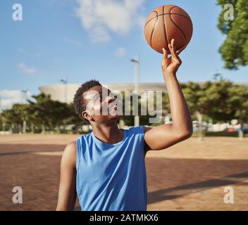 Porträt eines afroamerikanischen Basketballspielers, der seinen Ball auf der einen Seite vor dem Hintergrund der Stadt ausbalanciert Stockfoto
