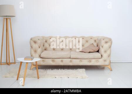 Beigefarbenes Sofa mit dekorativem Kissen, Couchtisch und Lampe im weißen Wohnzimmer. Wohnzimmer innen. Skandinavischer Stil Stockfoto