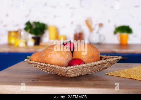 Korbkorb mit Äpfeln und Kürbissen in der Küche. Obst und Gemüse in Korbhalsgerichten auf dem Tisch im Speisesaal. Veganer, Vegetarismus. Stockfoto