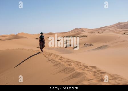 Frau, die in den Dünen in der marokkanischen Sahara-Wüste spazieren geht. Stockfoto