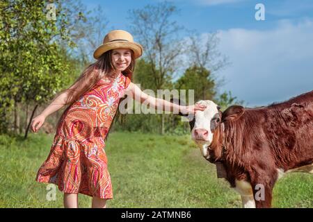 Kleines Mädchen streichelt auf einem Feld ein Kalb. Stockfoto