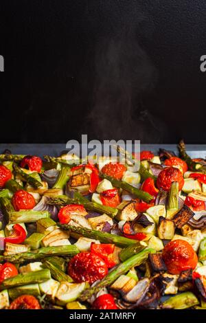 Heiß geröstetes Gemüse im Ofen. Gemischte Scheiben Spargel, Tomaten, Kürbis, Zwiebel und Olivenöl in einem Backblech Stockfoto