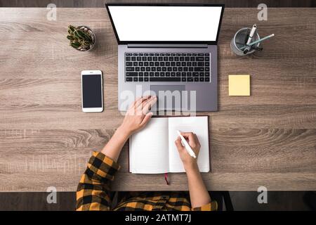 Top View Hände einer Geschäftsfrau, Studentin oder Freiberuflerin in gelbem Hemd mit Laptop weißen Bildschirm mit und macht Notizen. Weißer Bildschirm Stockfoto